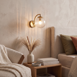 Curved Arm Ball Sconce in brass, lit above an oak bench with pampas grass
