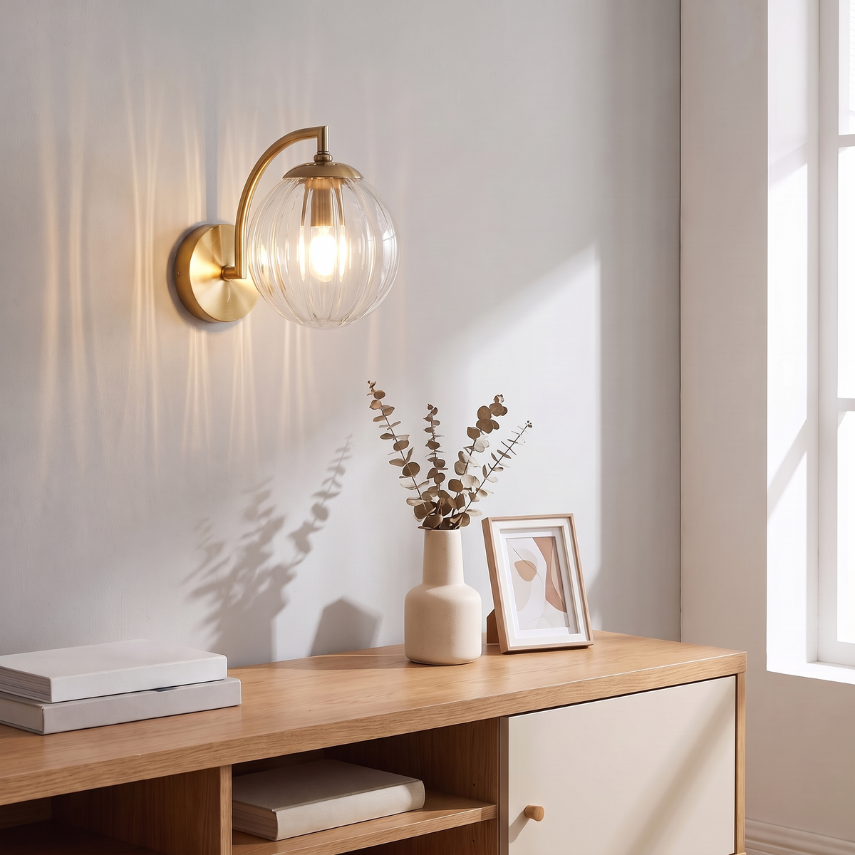 Curved Arm Ball Sconce in brass on a sunlit wall above an oak console
