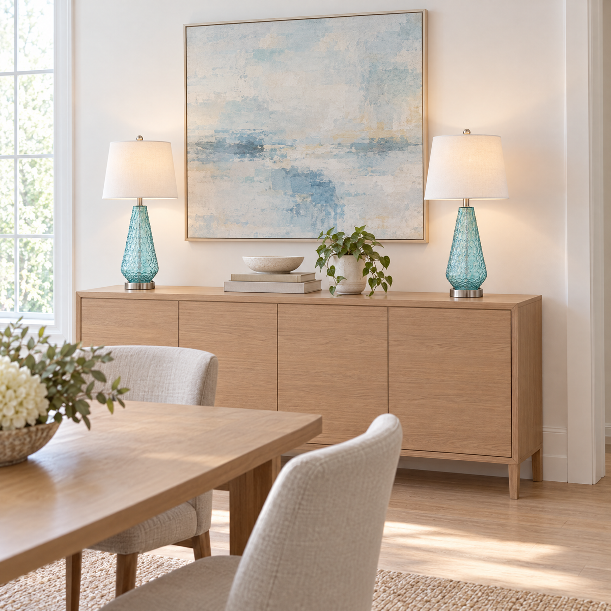 Pair of blue glass table lamps on a light oak sideboard in a modern dining room