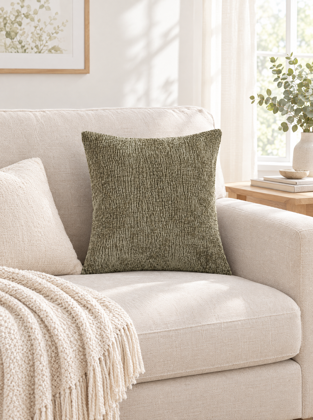 Dark sage jacquard pillow cover on a cream sofa with a fringed knit throw in a bright living room