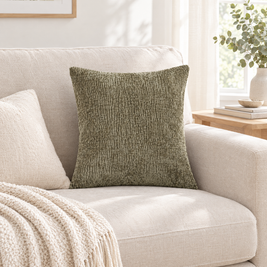 Dark sage jacquard pillow cover on a cream sofa with a fringed knit throw in a bright living room